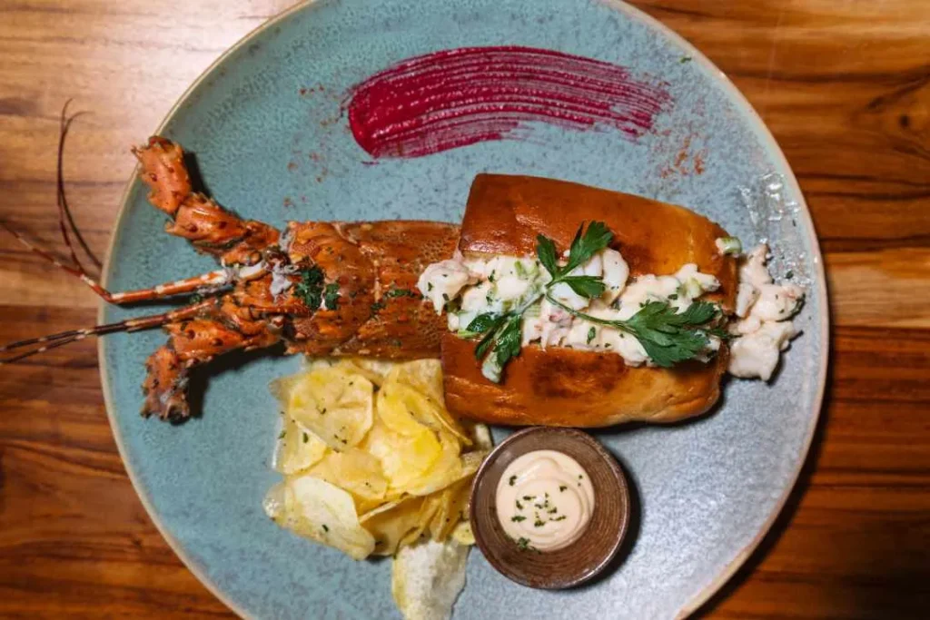Beautifully plated lobster roll in toasted brioche bun with potato chips and dipping sauce.