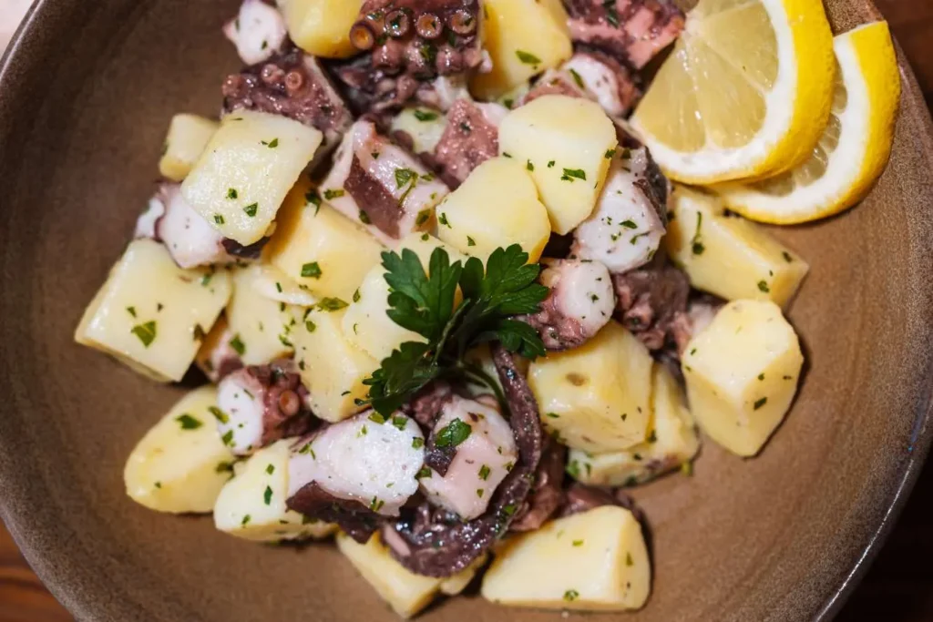 Chilled octopus and potato salad garnished with lemon slices and fresh parsley at KAIO Beach Front.