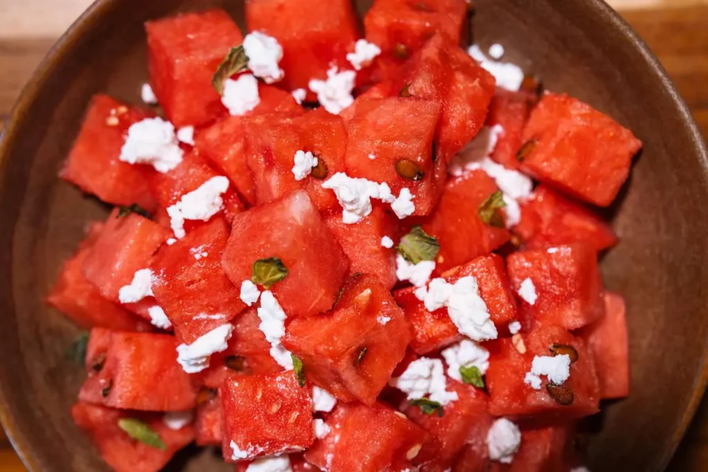 Close-up watermelon cubes topped with crumbled feta cheese and mint in a bowl at KAIO Beach Front.